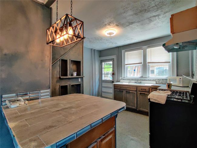 Kitchen featuring tile counters, light brown cabinets, under cabinet range hood, stainless steel gas stove, and white microwave | Image 14