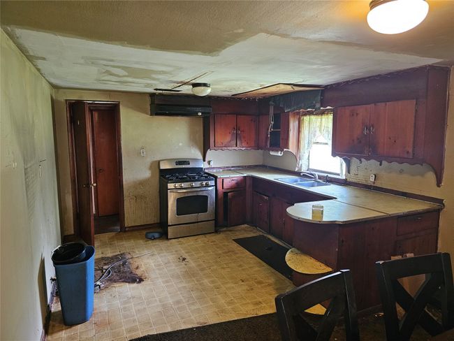 Kitchen featuring gas range, a peninsula, light flooring, light countertops, and extractor fan | Image 7