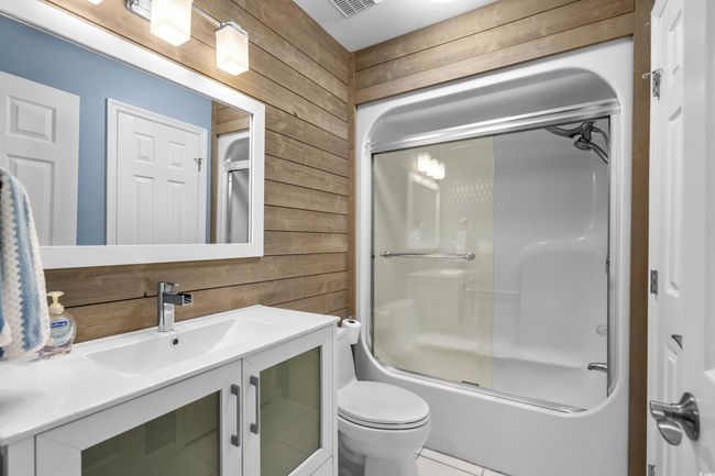 Full bathroom with wooden walls, toilet, vanity, combined bath / shower with glass door, and tile patterned floors | Image 15