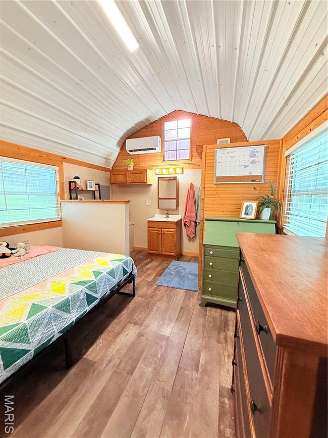 Bedroom featuring a wall mounted air conditioner, vaulted ceiling, light wood-style floors, wood walls, and a sink | Image 18