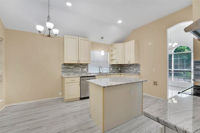 Kitchen featuring decorative light fixtures, tasteful backsplash, light stone counters, a center island, and stainless steel dishwasher | Image 10