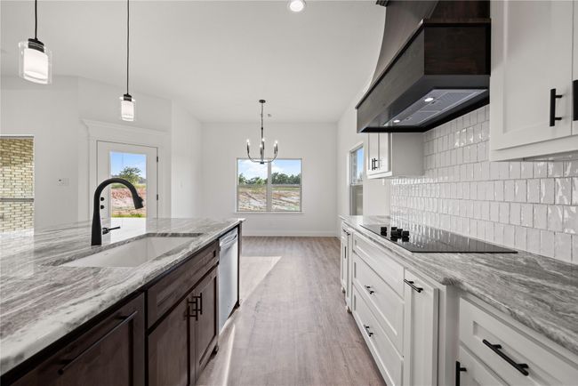 Kitchen with black electric cooktop, wall chimney exhaust hood, a sink, backsplash, and dark brown cabinetry | Image 17