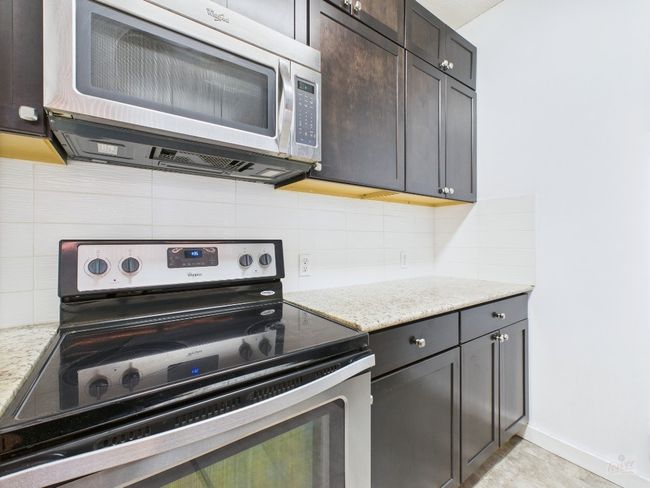 Kitchen featuring appliances with stainless steel finishes, tasteful backsplash, light stone counters, and dark brown cabinets | Image 12