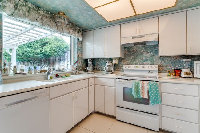 Kitchen with white appliances, under cabinet range hood, light countertops, and tasteful backsplash | Image 12