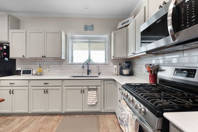 Kitchen with ornamental molding, a sink, stainless steel appliances, light wood-style floors, and light countertops | Image 8