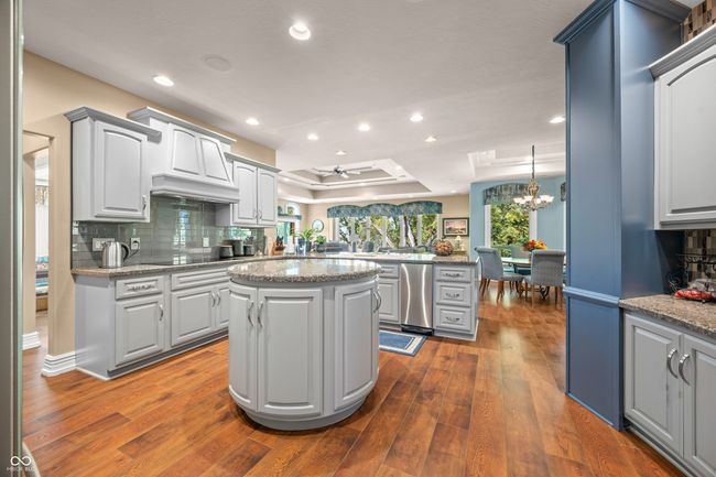 kitchen with decorative backsplash, ceiling fan with notable chandelier, dark wood-style floors, a center island, and a raised ceiling | Image 34