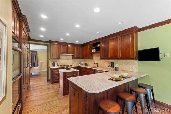 Kitchen with a peninsula, a kitchen breakfast bar, light wood-style floors, decorative backsplash, and open shelves | Image 18