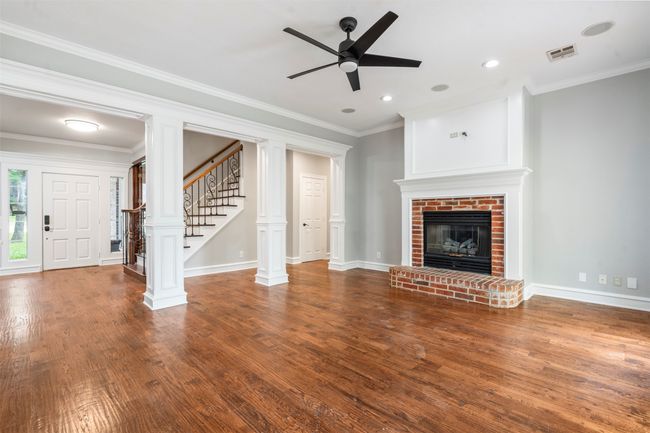 Unfurnished living room with stairway, a ceiling fan, wood finished floors, a brick fireplace, and crown molding | Image 16