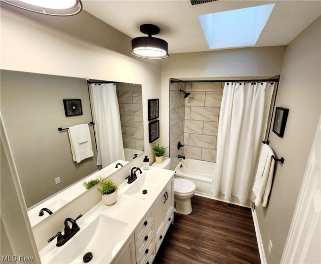 Full bathroom featuring hardwood / wood-style flooring, shower / tub combo, dual vanity, toilet, and a skylight | Image 15