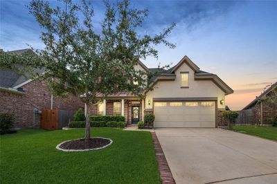 This is a two story home with a well-maintained lawn and a mature tree in the front yard. It features a two-car garage, brick facade, and a welcoming entryway. | Image 1