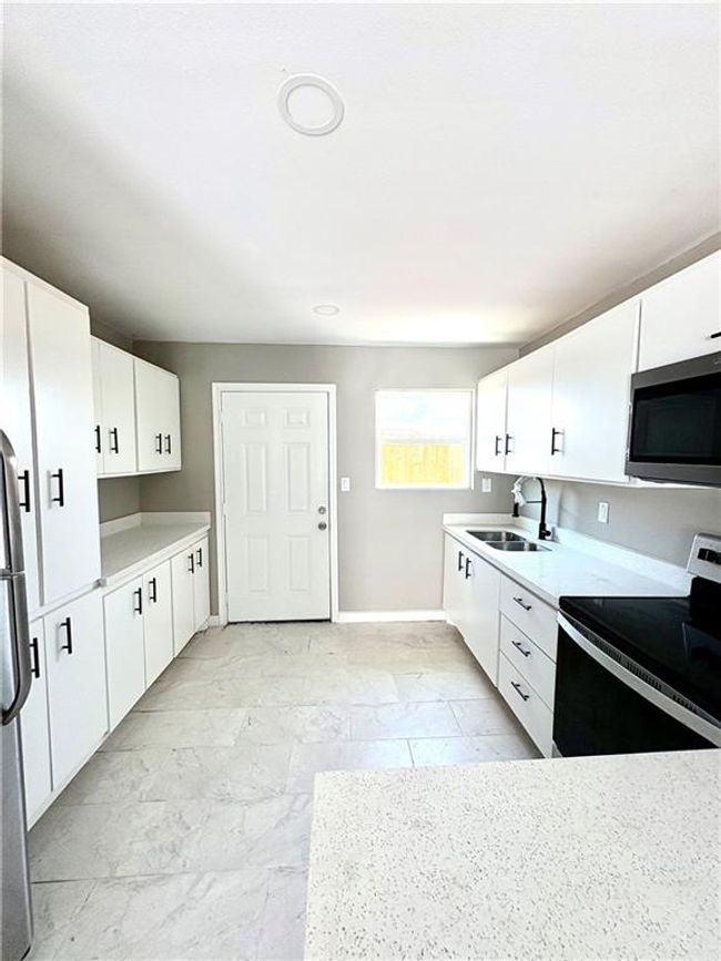 Kitchen featuring stainless steel appliances, white cabinetry, light countertops, and light marble finish floors | Image 4
