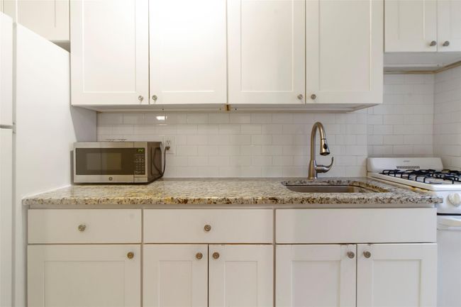 Kitchen with white appliances, decorative backsplash, white cabinetry, and light stone counters | Image 7