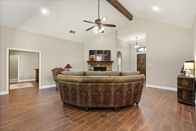 Living room featuring a ceiling fan, high vaulted ceiling, arched walkways, a stone fireplace, and beamed ceiling | Image 4