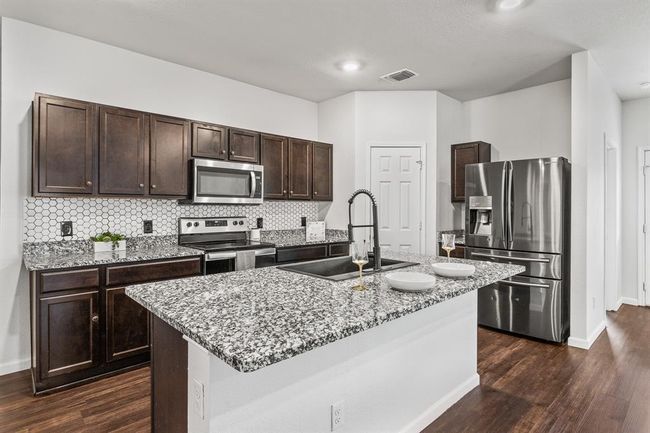 Kitchen featuring appliances with stainless steel finishes, dark wood-style flooring, dark brown cabinets, light stone countertops, and recessed lighting | Image 6