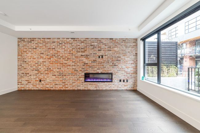 Unfurnished living room with dark wood-type flooring, plenty of natural light, a brick fireplace, brick wall, and a raised ceiling | Image 12