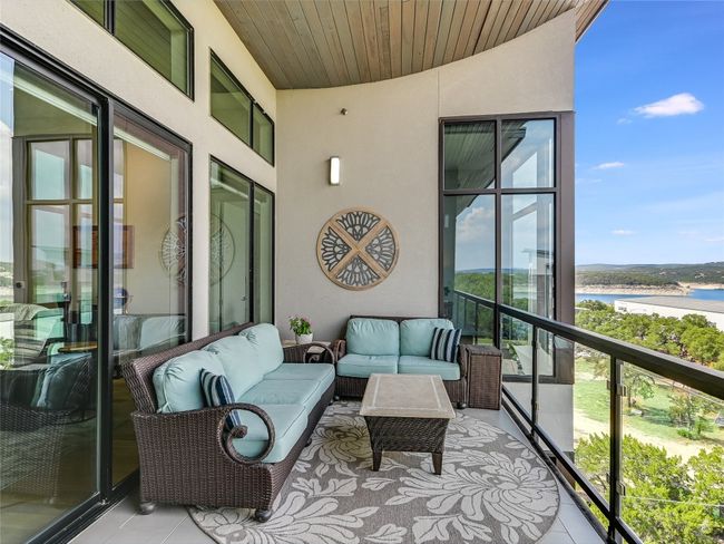 Sliding glass doors lead you outside to a spacious covered balcony highlighted by an upward-curving raised wood-planked ceiling and glass railing. | Image 23