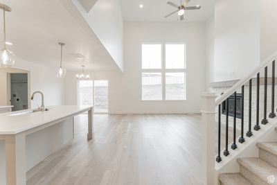 Unfurnished living room with sink, light hardwood / wood-style flooring, ceiling fan with notable chandelier, and a high ceiling | Image 3