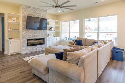 Living room with ceiling fan, a stone fireplace, hardwood / wood-style flooring, and built in shelves | Image 2