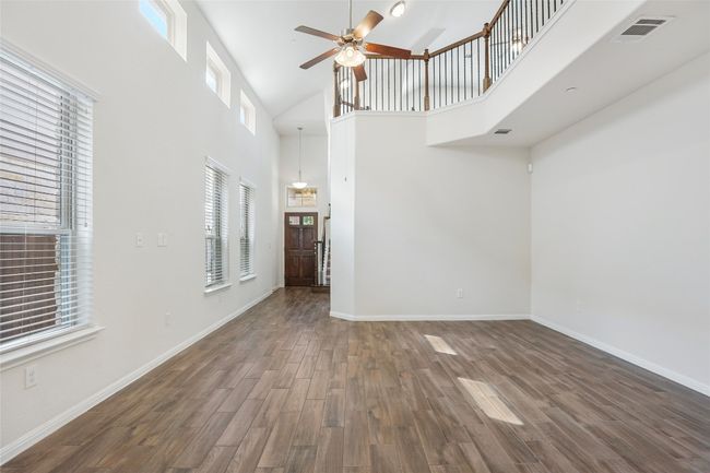 Unfurnished living room with baseboards, visible vents, wood finished floors, a high ceiling, and ceiling fan | Image 4