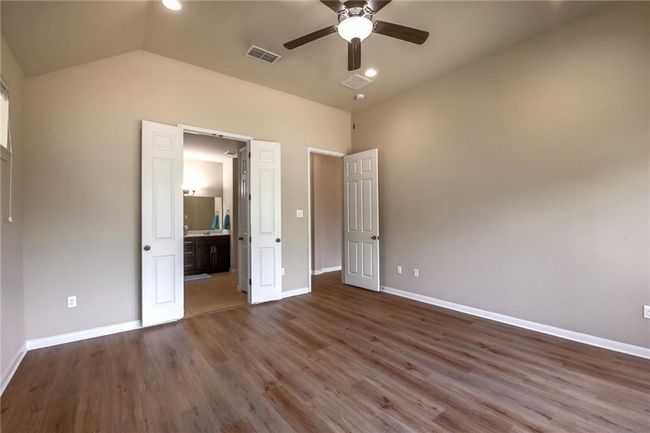 Unfurnished bedroom featuring vaulted ceiling, wood finished floors, ensuite bath, and a ceiling fan | Image 16