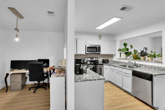 Kitchen featuring stainless steel appliances, light stone countertops, light wood-style flooring, and white cabinets | Image 13