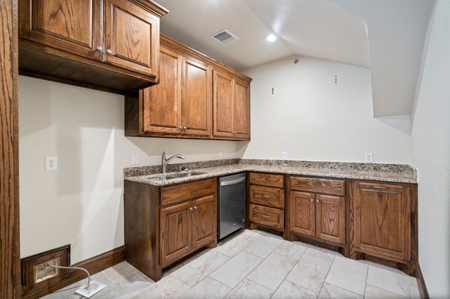 Upstairs Kitchen with dishwasher, vaulted ceiling, light stone counters, brown cabinetry, and light marble finish flooring | Image 15