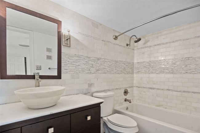 Bathroom featuring shower / bathtub combination, tile walls, toilet, vanity, and decorative backsplash | Image 13