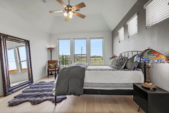Bedroom with lofted ceiling, multiple windows, a textured wall, wood finished floors, and a ceiling fan | Image 19