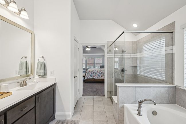 Ensuite bathroom featuring a garden tub, dual sink, vanity, a shower stall, lofted ceiling, custom mirror, linen closet, and dual sink | Image 25