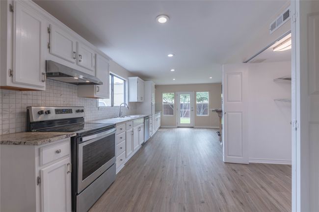 Kitchen with stainless steel appliances, under cabinet range hood, light wood-style flooring, white cabinetry, and recessed lighting | Image 4