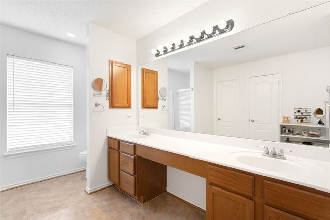 Full bath featuring double vanity, toilet, tile patterned flooring, baseboards, Primary full bath featuring double vanity, complemented by fresh paint, a separated shower, a jetted tub, and an oversized walk-in closet.and a textured ceiling | Image 31