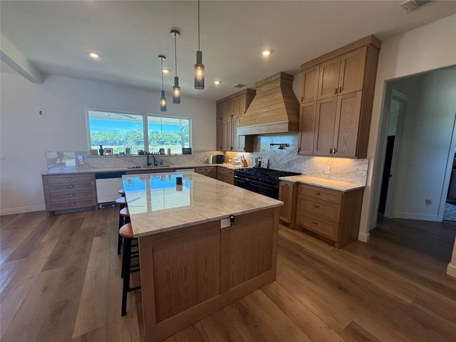 Kitchen featuring custom exhaust hood, light countertops, a kitchen island, dark wood-type flooring, and decorative backsplash | Image 20