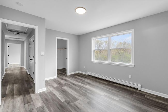 Unfurnished bedroom featuring a baseboard heating unit, baseboards, a spacious closet, and dark wood finished floors | Image 28