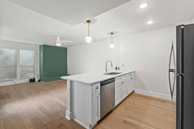 Kitchen featuring stainless steel dishwasher, freestanding refrigerator, a peninsula, a sink, and light wood finished floors | Image 13