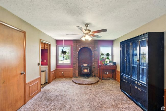 Carpeted living area featuring a wood stove, a wainscoted wall, a ceiling fan, and a textured ceiling | Image 8