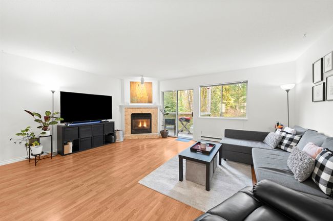 Living room featuring a warm lit fireplace, baseboards, light wood-style floors, and baseboard heating | Image 15