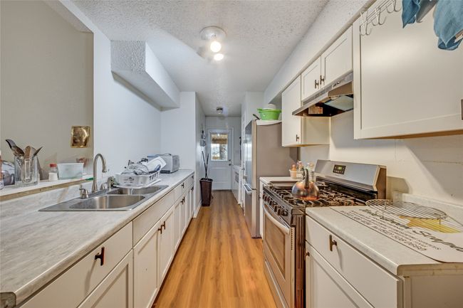 Unit A Kitchen featuring sink, stainless steel range with gas stovetop, light hardwood / wood-style flooring, a textured ceiling, and white cabinets | Image 29