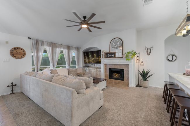 Living room featuring a ceiling fan, a tiled fireplace, arched walkways, lofted ceiling, and baseboards | Image 15