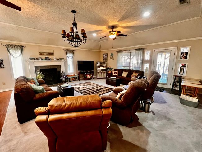 Carpeted living room with a healthy amount of sunlight, lofted ceiling, a textured ceiling, a fireplace, and ornamental molding | Image 15