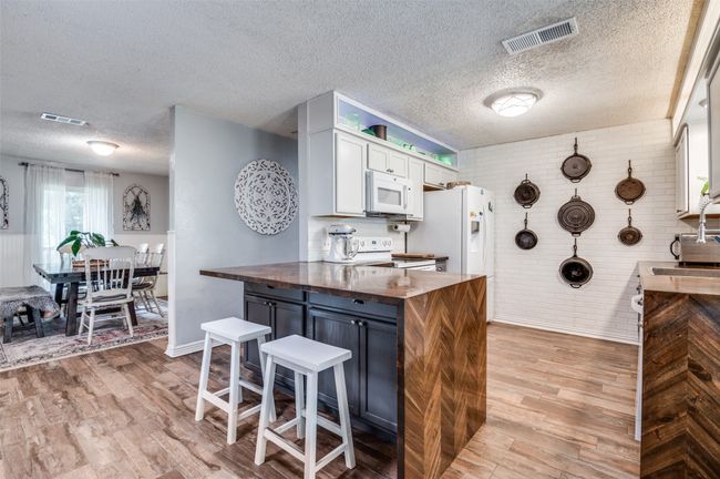 Kitchen with white appliances, butcher block countertops, light wood-type flooring, a textured ceiling, and white cabinets | Image 10