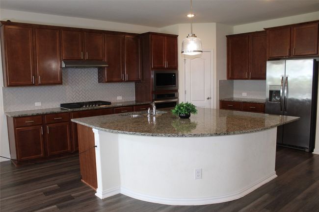 Kitchen featuring stainless steel appliances, dark wood-style floors, a sink, a kitchen island with sink, and decorative backsplash | Image 30