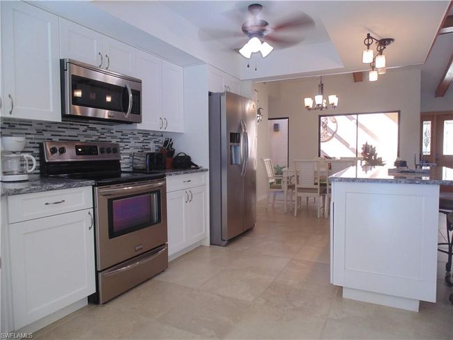 Kitchen featuring dark stone countertops, decorative backsplash, white cabinets, appliances with stainless steel finishes, and ceiling fan with notable chandelier | Image 8