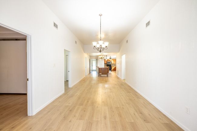 Hall featuring light wood-style flooring, an inviting chandelier, baseboards, and visible vents | Image 5