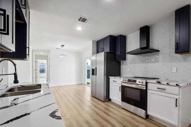 Kitchen featuring light wood-style flooring, visible vents, white cabinets, appliances with stainless steel finishes, and wall chimney exhaust hood | Image 10