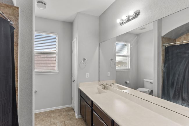 Lovely secondary bathroom complete with a large mirror, granite countertops and wooden cabinets, and a shower/tub combo with a gorgeous tile shower wall. | Image 17
