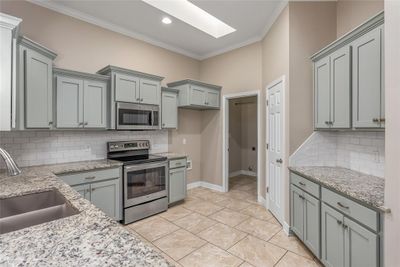 Kitchen with light stone counters, stainless steel appliances, backsplash, a skylight, and ornamental molding | Image 2