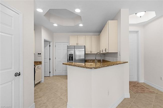Kitchen featuring stainless steel fridge, dark stone countertops, light tile patterned floors, a peninsula, and recessed lighting | Image 6