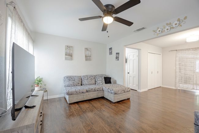 Living room with wood finished floors, baseboards, a ceiling fan, and visible vents | Image 4