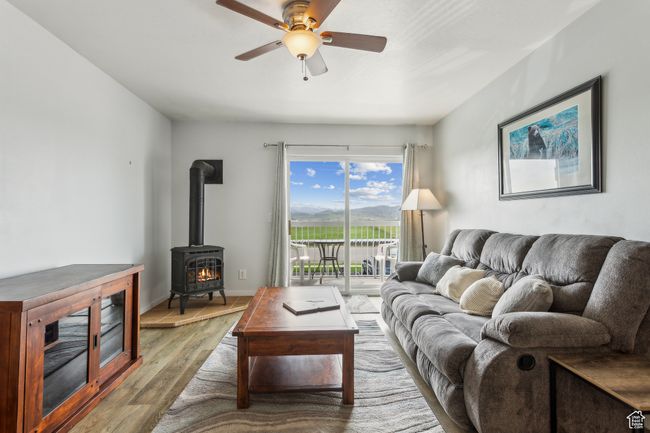Living area with wood finished floors, a wood stove, ceiling fan, and baseboards | Image 6