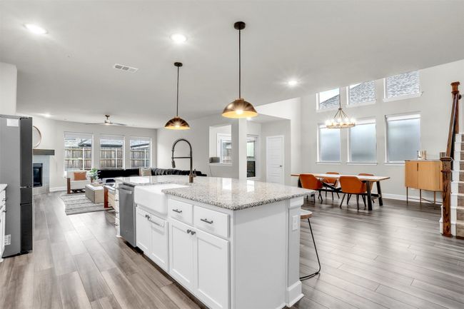 Kitchen featuring visible vents, a sink, a glass covered fireplace, stainless steel appliances, and a kitchen island with sink | Image 8